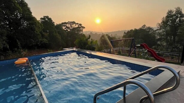 A swimming pool at sunset with a slide, surrounded by trees and a clear sky. - Hillock Vista Homestay by Aarika Resorts (Sakleshpur)