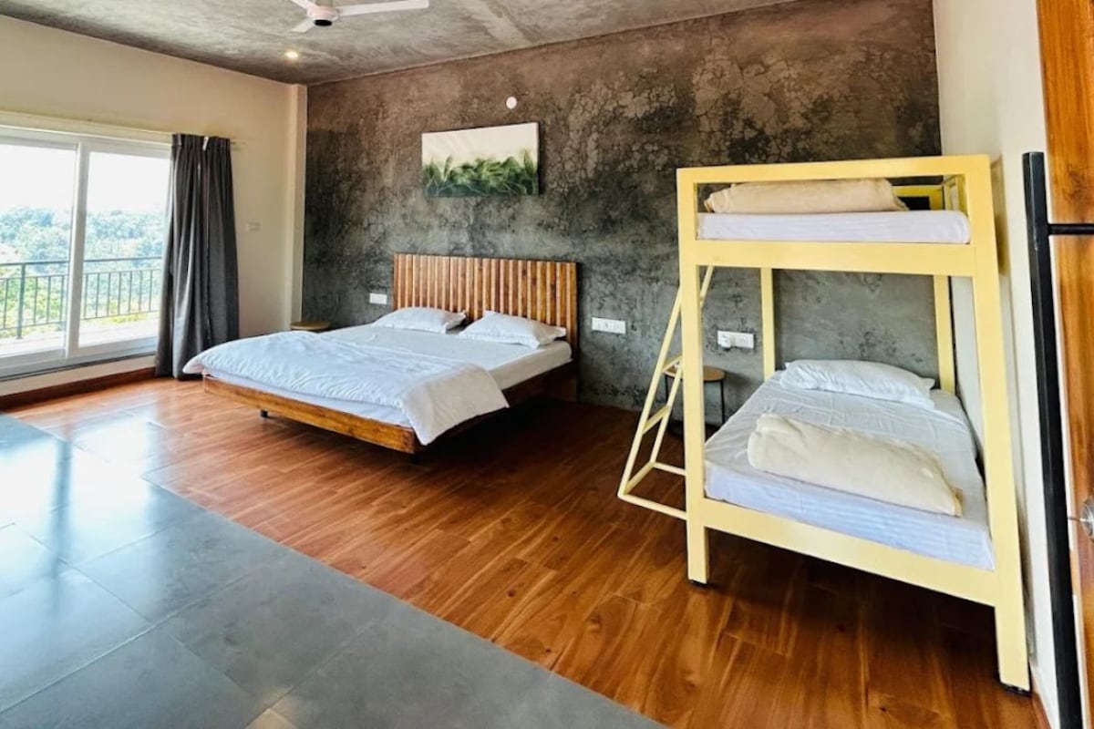A bedroom with a bunk bed, a ceiling fan, a large window, and a view of the outdoors.