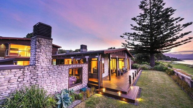 A modern house with a stone facade, large windows, and a deck overlooking a grassy area. - Tata Tides Beach Front Retreat - Golden Bay at its finest (Tata Beach)