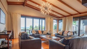 A spacious living room with leather sofas, a wooden coffee table, and large windows offering a view of the outdoors. - Tata Tides Beach Front Retreat - Golden Bay at its finest (Tata Beach)