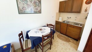 A small kitchen with wooden cabinets, a sink, and a stove. There is a dining table with chairs and a decorative map on the wall. - Studio Nadica (Šmrika)