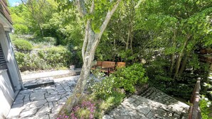 A stone-paved courtyard with a wooden bench, surrounded by lush greenery and flowering plants. - Studio Nadica (Šmrika)