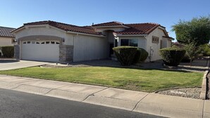 A single-story house with a garage, a well-maintained lawn, and a clear blue sky. - Active Adult Escape in Trilogy – Golf, Fitness, Pools & More! (Gilbert)