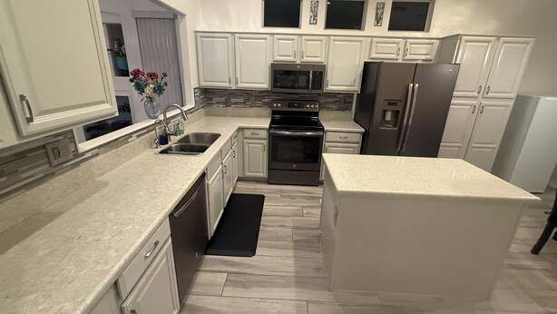 A modern kitchen with white cabinets, stainless steel appliances, and a black rug on the floor. - Active Adult Escape in Trilogy – Golf, Fitness, Pools & More! (Gilbert)