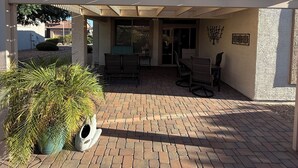 A covered patio area with brick flooring, outdoor furniture, and a pergola structure. - Active Adult Escape in Trilogy – Golf, Fitness, Pools & More! (Gilbert)