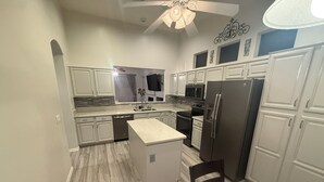 A modern kitchen with white cabinetry, a central island, stainless steel appliances, and a ceiling fan. - Active Adult Escape in Trilogy – Golf, Fitness, Pools & More! (Gilbert)