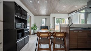 Une cuisine moderne avec des meubles de couleur sombre, un coin repas avec des chaises en bois et une grande fenêtre qui laisse entrer la lumière naturelle.