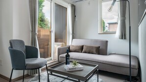 Un salon moderne avec un canapé, un fauteuil, une table basse sur laquelle se trouvent une bouteille et un objet décoratif, ainsi qu  ’une grande fenêtre avec des rideaux.
