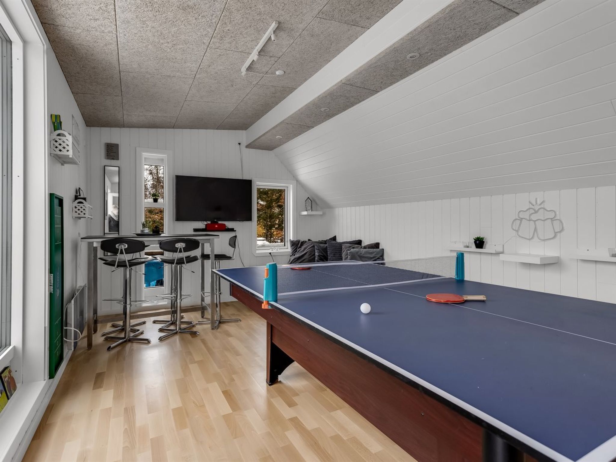 A room with a ping pong table, a TV, a bar area, and a window with a view.