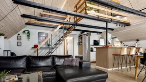 Un espace de vie moderne comprenant un canapé d’angle en cuir noir, une table basse en verre et un coin repas en bois avec des tabourets de bar.
