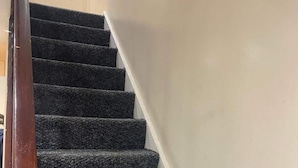 Una escalera con peldaños cubiertos de moqueta oscura y barandilla blanca.
