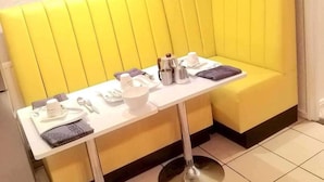 Un mostrador amarillo con una mesa blanca, equipado con una cafetera, tazas y una cuchara.