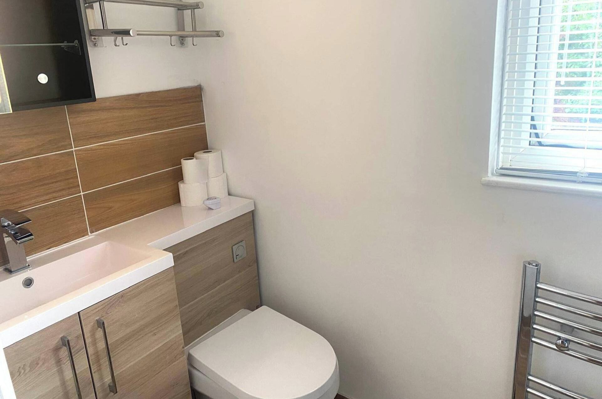 Un baño moderno con un mueble de tocador de madera, un inodoro y una ventana con persianas.