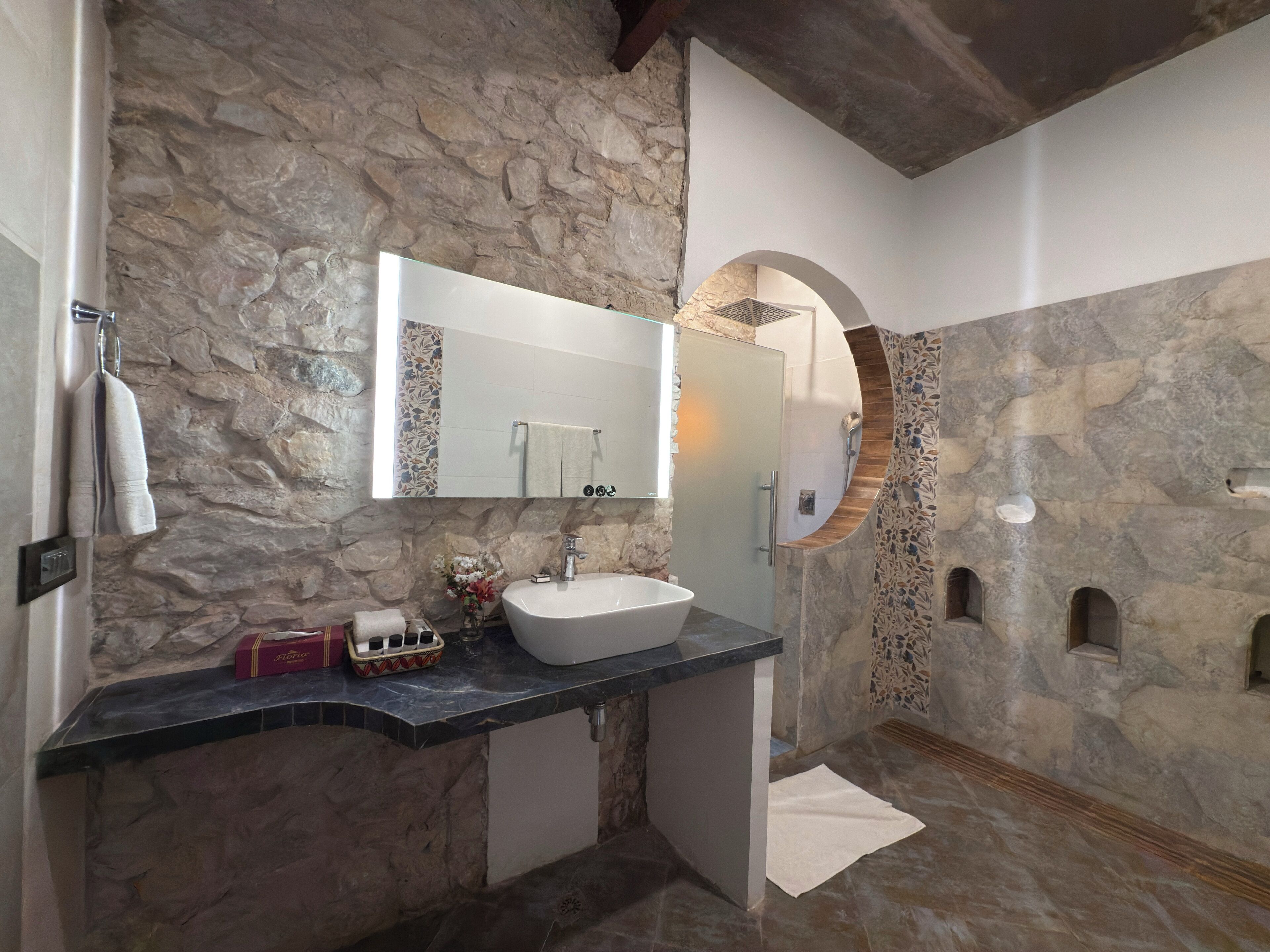 Une salle de bain avec un mur en pierre, un lavabo blanc et un miroir.