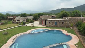 A swimming pool with a wooden deck and a stone wall. - Sariska Kasba - A Village Resort (Rajgarh)