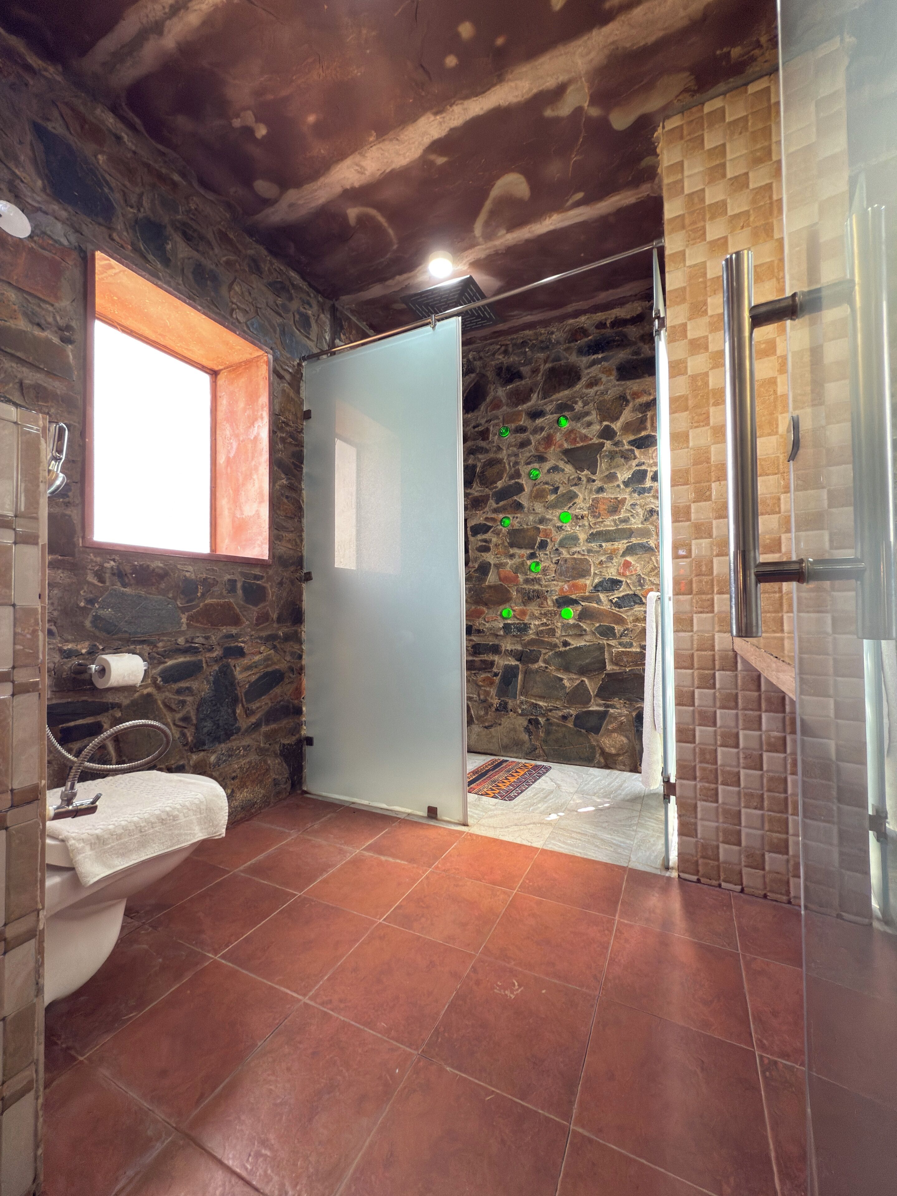 Un baño con pared de piedra, ventana, lavabo y zona de ducha.