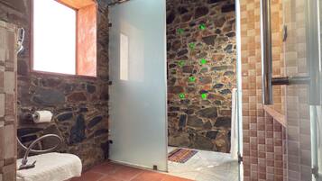 Un bagno con parete in pietra, una finestra, un lavandino e cabina doccia.