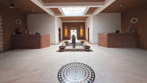 A spacious lobby with a high ceiling, a central decorative area with a statue, and a patterned floor. - Sariska Kasba - A Village Resort (Rajgarh)