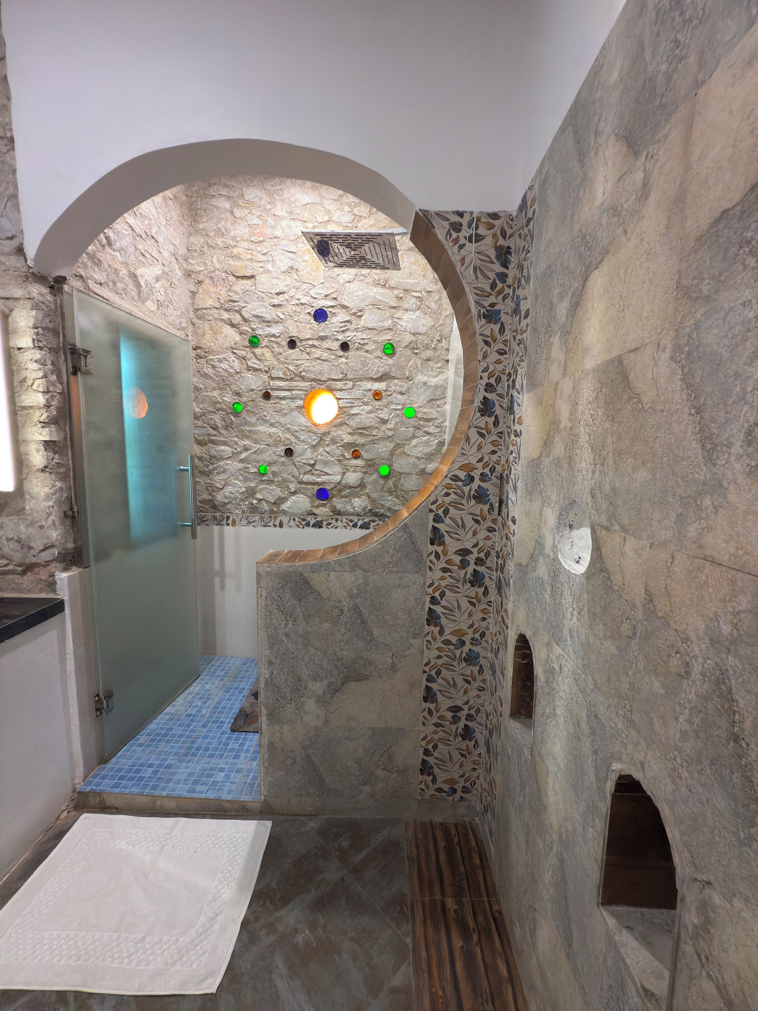Une salle de bain avec un mur en pierre, une douche en verre et un sol carrelé à motifs.