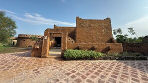 A historic building with a stone facade, a central doorway, and a paved courtyard. - Sariska Kasba - A Village Resort (Rajgarh)