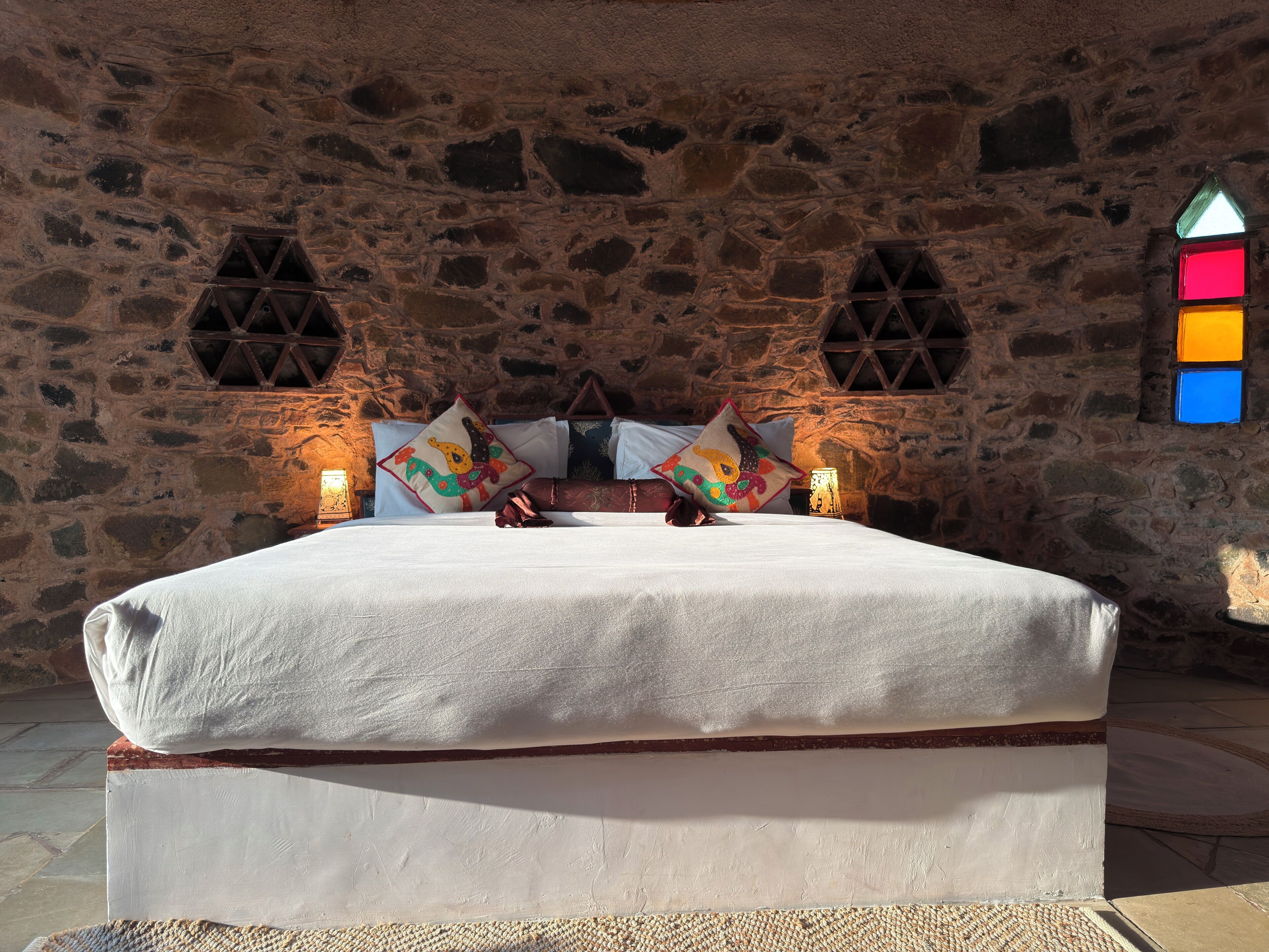 Una stanza con pareti in pietra, un letto, due cuscini e un punto luce a parete.