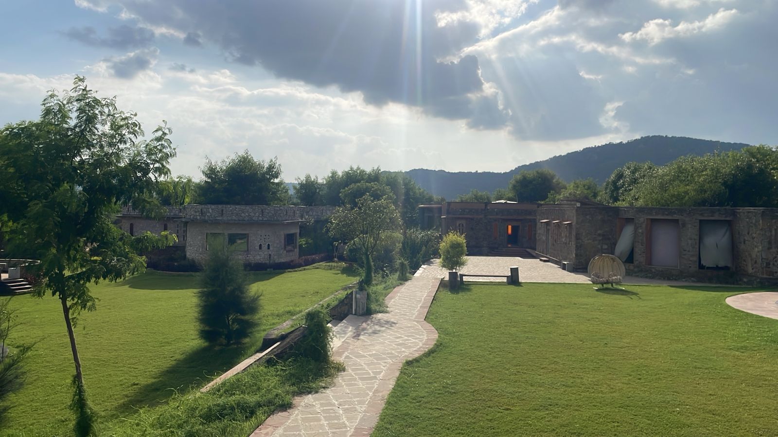 A courtyard with stone buildings, a paved pathway, and a grassy area.