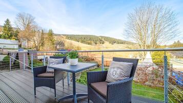 Eine Terrasse mit Korbmöbeln und einem Tisch, mit Blick auf eine reizvolle Landschaft mit Hügeln und Bäumen.