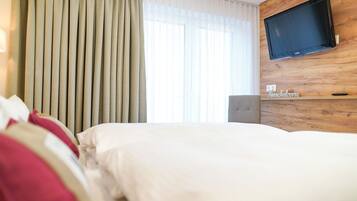 Ein Hotelzimmer mit Bett, einem an einer Holzwand montierten Fernseher und einem Fenster mit Vorhängen.