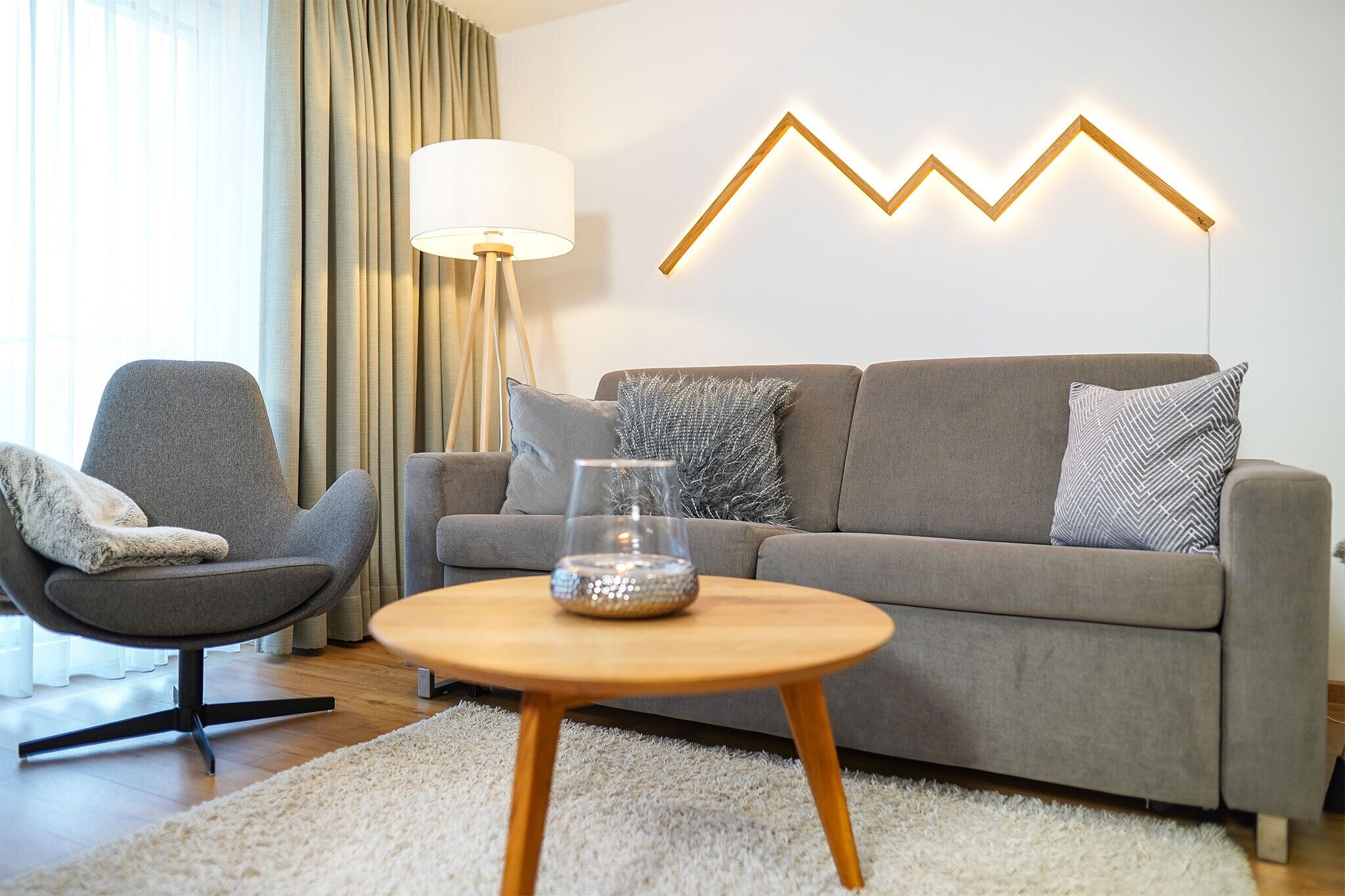 Ein modernes Wohnzimmer mit einem grauen Sofa, einem runden Couchtisch und einer Lampe.