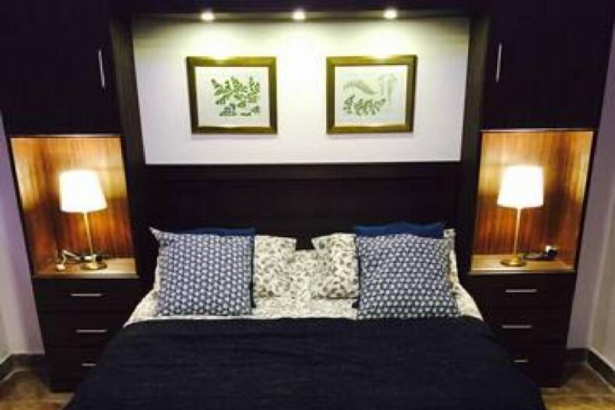 Ein Schlafzimmer mit einem großen Bett, zwei Nachttischen, einer Bank und gerahmten Bildern an der Wand.