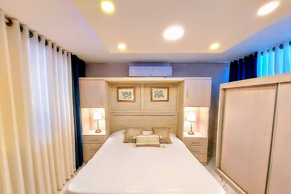Ein Hotelzimmer mit einem großen Bett, Nachttischlampen, einem Kopfteil mit Klimaanlage und einem Fenster mit Vorhängen.