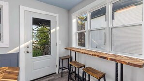 A narrow hallway with a white door, a window with blinds, and a wooden bench. - Rink Side Retreat (Grand Rapids)