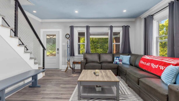 A modern living room with a staircase, a leather sofa, a coffee table, and a view of the outdoors. - Rink Side Retreat (Grand Rapids)