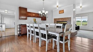 Un grand espace de salle à manger avec une table en bois et des chaises blanches, une cuisine avec des meubles en bois et une cheminée.