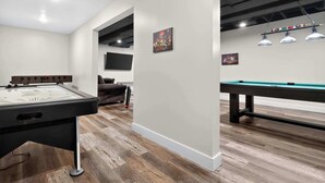 Une salle de billard équipée d’une table de billard américain, d’une table de snooker et d’un canapé.