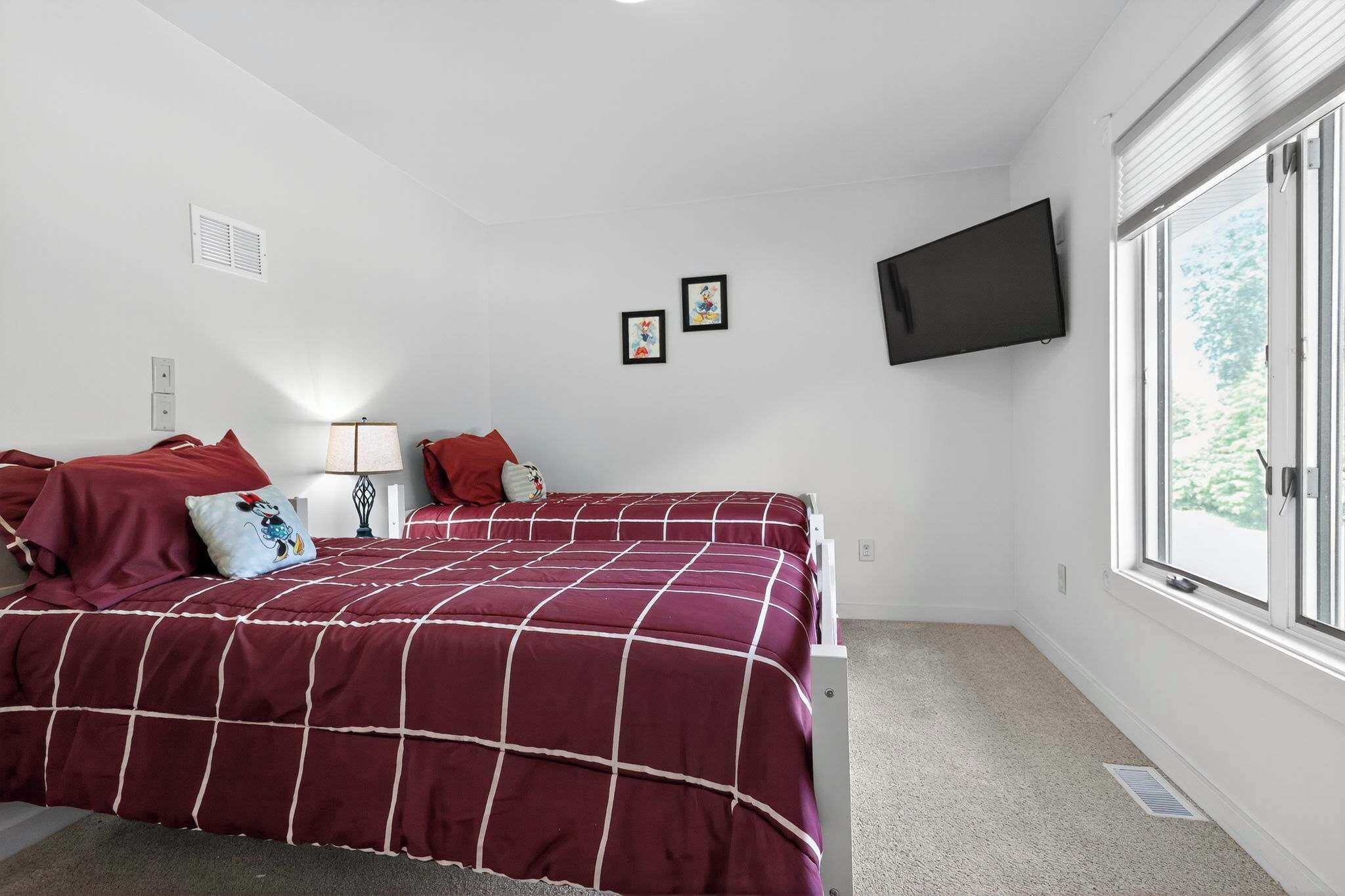 Ein Schlafzimmer mit einem großen Bett, einem an der Wand montierten Fernseher und einem Fenster mit Jalousien.