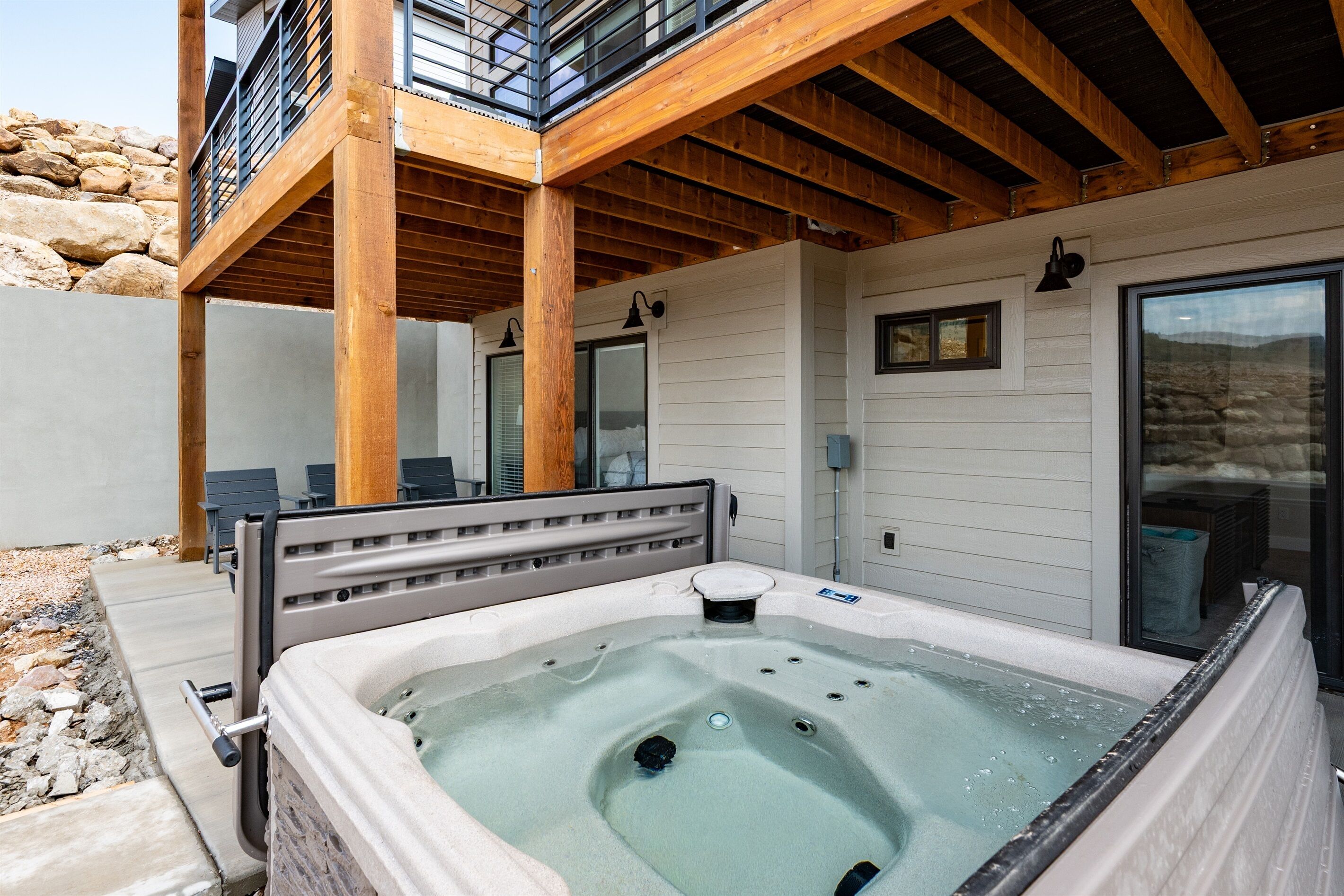 A hot tub with a wooden deck and stone wall backdrop.