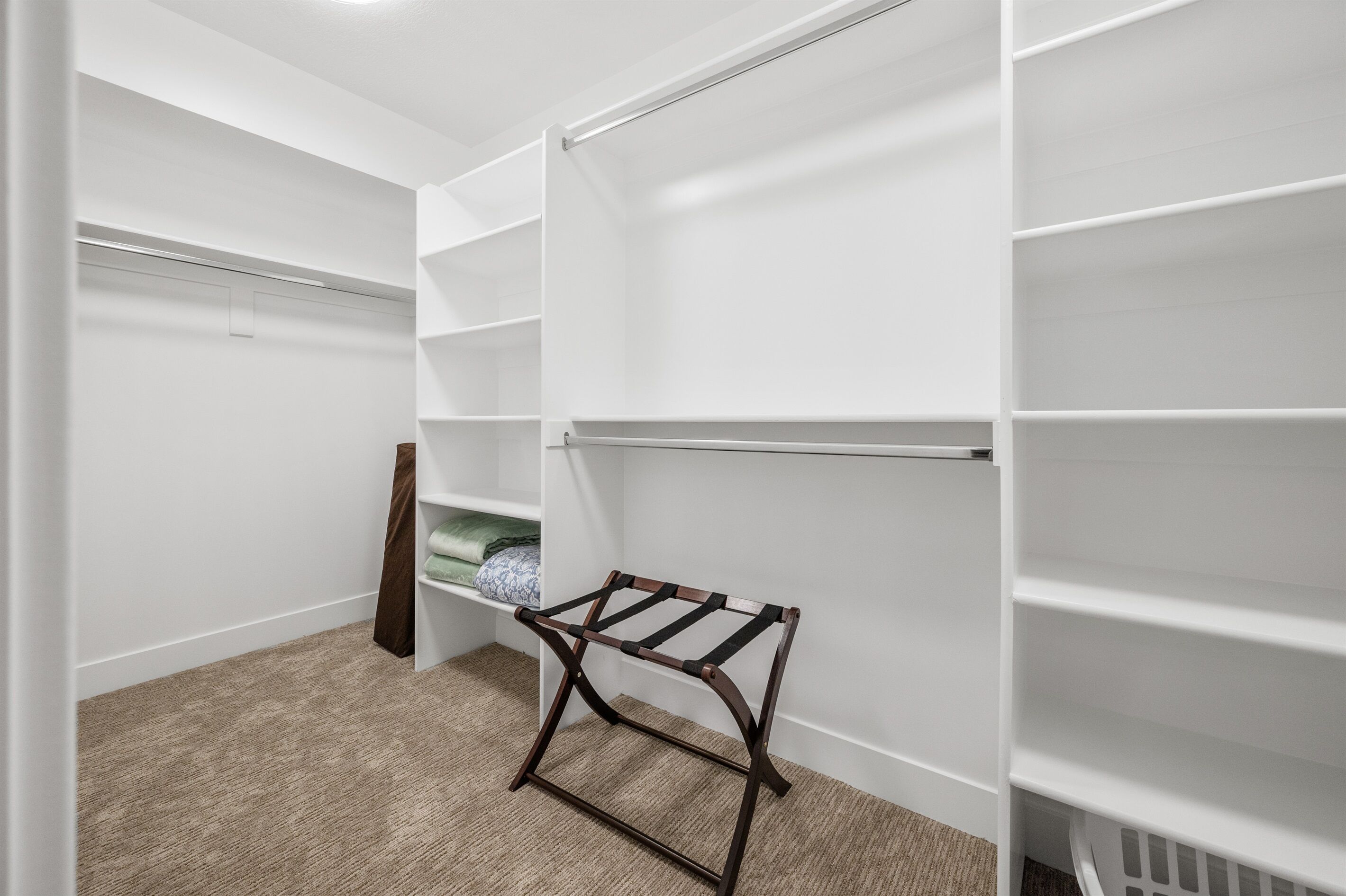Um closet espaçoso com prateleiras brancas, um varal de madeira e piso coberto por carpete.