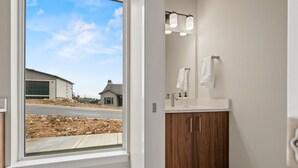 Ein Badezimmer mit großem Fenster, Holzschränken, einer weißen Arbeitsplatte und einem Spiegel mit Beleuchtung.