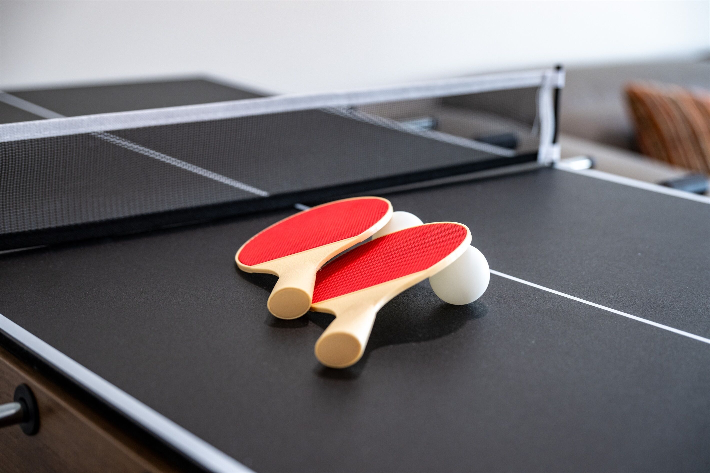 Une table de ping-pong avec deux raquettes rouges et une balle blanche.