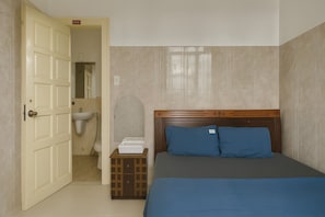A bedroom with a bed, a wooden headboard, a nightstand, a white sink, and a door leading to a bathroom. - Viet Ha Hotel (Da Lat)