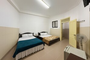 A hotel room with two single beds, a bedside table, a small table, a fan, and a door leading to a bathroom. - Viet Ha Hotel (Xuan Huong - Da Lat)