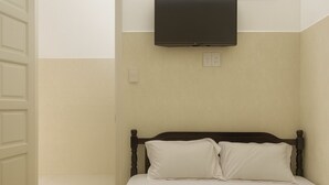 Quarto de hotel com uma cama, uma TV de tela plana acima dela e uma porta à esquerda.