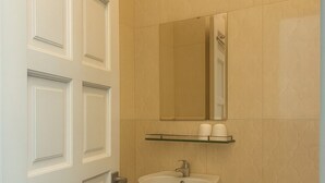 Um banheiro com porta branca, pia, espelho e vaso sanitário.