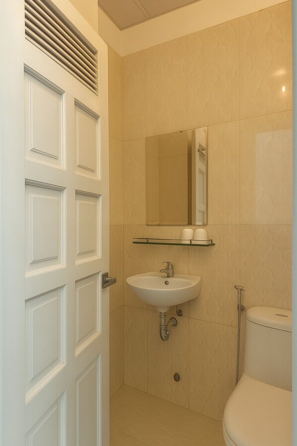 A bathroom with a white door, a sink, a mirror, and a toilet. - Viet Ha Hotel (Da Lat)