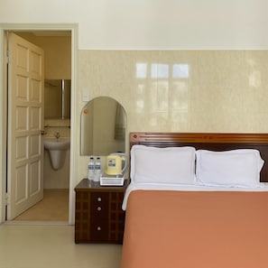 A hotel room with a bed, a bedside table with toiletries, a mirror, and a bathroom visible through an open door. - Viet Ha Hotel (Da Lat)