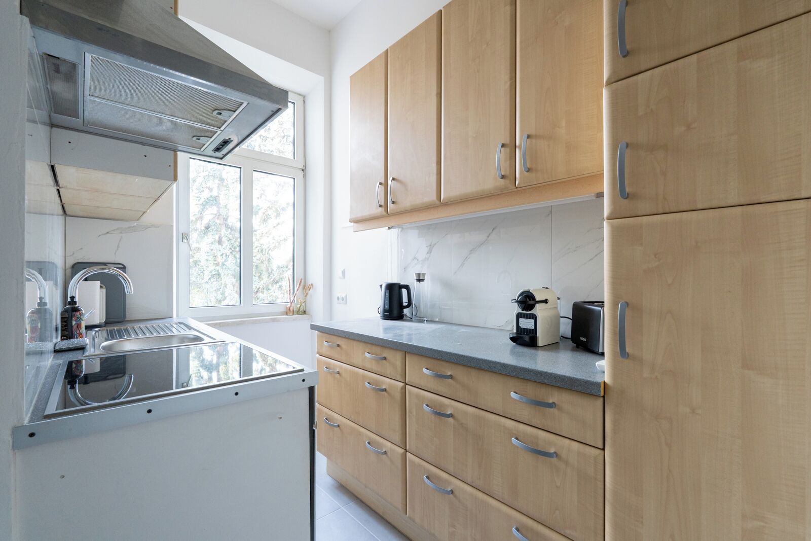 Una cocina moderna con un lavamanos de acero inoxidable, armarios de madera y un ventanal que proporciona luz natural.
