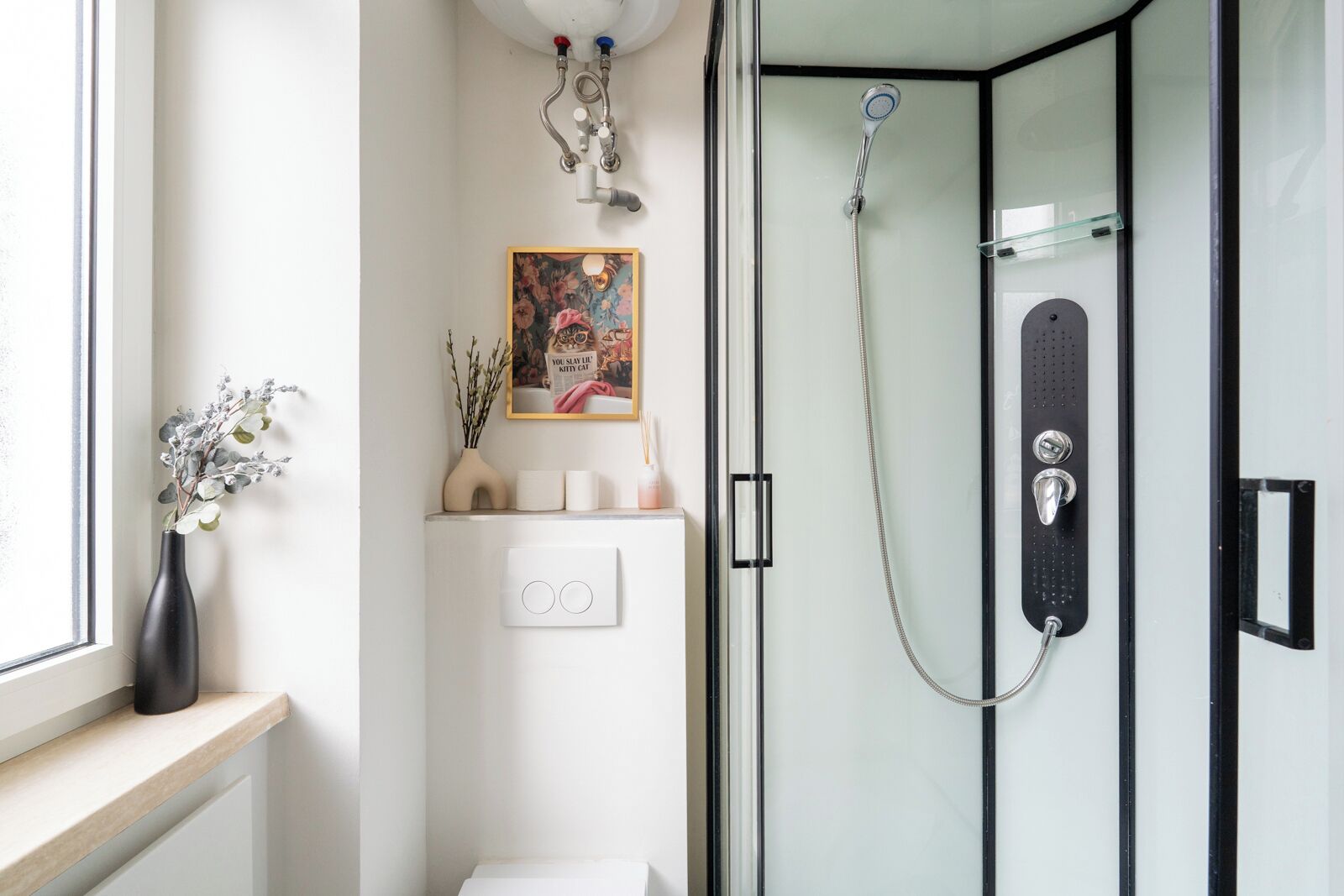 Ein modernes Badezimmer mit Duschkabine aus Glas, Toilette, Waschbecken und einem Fenster mit Blumen in einer Vase.