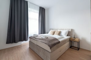 Ein modernes Schlafzimmer mit einem großen Bett, einem Nachttisch und einem Fenster mit Vorhängen.