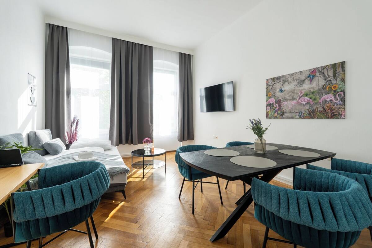 Ein modernes Wohnzimmer mit einer Couch, einem Esstisch mit Stühlen, einem an der Wand montierten Fernseher und einem Gemälde.